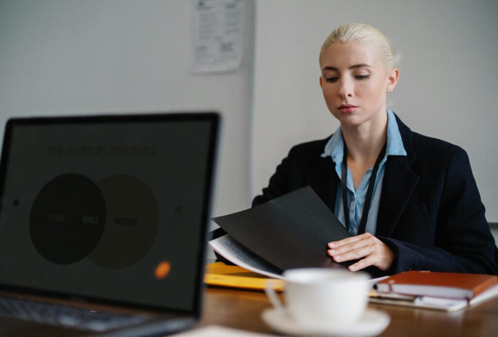 Professional company secretary managing administrative tasks at a desk, with paperwork, a laptop, and filing cabinets in a corporate office.